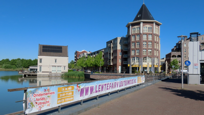 912839 Afbeelding van een lang spandoek met o.a. de tekst 'WWW.LENTEFAIRVLEUTERWEIDE.NL' op een reling langs het water ...